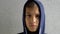 Teenage boy in navy hooded jacket raises his head and looking directly to camera. Calm, serious, sad, contemplative kid