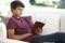 Teenage Boy Relaxing On Sofa At Home Reading Book