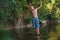 A teenage boy in shorts plays in a mountain river in shallow water