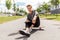 Teenage boy sitting on skateboard on city street