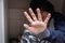 A teenage boy sitting under the table and hiding his face with a hand