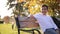 Teenage boy in white sweater sitting on the bench. Handsome school boy with backpack in autumn park