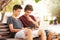 Teenage Boys On Park Bench Using Laptop And Digital Tablet