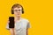 Teenage brunet boy with glasses wears headphones and holds smartphone with blank black screen. Copy space. Mock up