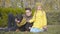 Teenage Caucasian boy in eyeglasses and his sister in yellow coat sitting on green grass with beautiful doberman in