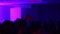 Teenage crowd is dancing in night club. Person raises hands enjoying the music