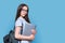 Teenage female student with backpack laptop on blue color background