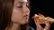 Teenage girl biting and eating slice of unhealthy pizza with meat and vegetables