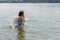 Teenage girl in blue swimsuit bathes in calm cool lake water in hot summer, raising a lot of splashes