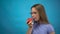Teenage girl with braces on her teeth eats a red tomato on a blue background. Girl with colored braces bites off a