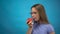 Teenage girl with braces on her teeth eats a red tomato on a blue background. Girl with colored braces bites off a