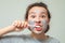 A teenage girl with a cosmetic mask on her face brushes her teeth. Facial scrub mask