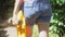 A teenage girl in denim shorts and an orange t-shirt carries a yellow skateboard in her hands. The girl walks along the