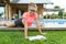 Teenage girl in glasses reads a book, background swimming pool, lawn near the house. School, education, knowledge, adolescents.
