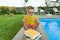 Teenage girl in glasses reads a book, background swimming pool, lawn near the house. School, education, knowledge, adolescents.