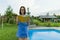 Teenage girl in glasses reads a book, background swimming pool, lawn near the house. School, education, knowledge, adolescents.