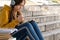 Teenage girl in headphones takes notes in a notebook, learns online sitting on the stairs in the park