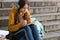 Teenage girl in headphones takes notes in a notebook, learns online sitting on the stairs in the park