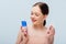 Teenage girl holding blue lotion and cotton pad isolated on grey