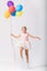 Teenage girl holding a bunch of balloons jumps in an empty room, copy space on the empty wall