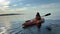 Teenage girl is kayaking at sunset in Pacific ocean, only the silhouette of kayak paddles is visible she swims along