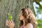 Teenage Girl Kissing Toy Frog Against Tree Trunk