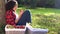 Teenage girl leaning against a tree in an orchard eating an apple using her mobile cell smart phone