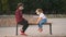 Teenage girl and little girl in social distancing sit on a park bench. Children in medical masks walk through the park
