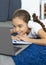 A teenage girl lying on the floor listening to the school program at home online in front of a laptop monitor. Vertical photo