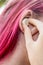 Teenage girl with ombre colored pink hair with wireless earbud earphone in her hand. Music phone calls podcast audiobooks