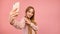 Teenage girl in pajamas taking selfies using the smartphone. Isolated on pink background