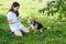 A teenage girl is playing with her dog beagle on the green grass under a flowering bird cherry bush