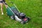 Teenage girl pruning green high grass with the help of an petrol lawn mower.