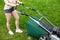 Teenage girl pruning green high grass with the help of an petrol lawn mower.