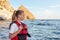 Teenage girl in red life jacket stands on ocean and looks at sea. Means of rescuing people on water, buoyancy and safety