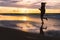 Teenage girl running barefoot on a sandy beach at sunset - a silhouetted photo of a young woman against the sky