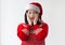 A teenage girl in a Santa Claus hat and a red Christmas sweater is surprised and holds her hands on her cheeks. The concept of