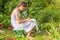 A teenage girl sits on a bench in the garden for her favorite pastime, drawing with a pencil in the album.