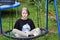 Teenage girl sits on a swing-spider web in the garden. Clothes depict a Japanese character.