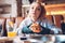 Teenage girl sitting in cafe, holding burger in hands