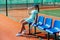 Teenage girl sitting on a chair bench next to tennis court to take a short break