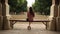 Teenage girl sitting down on bench in nature and reading a book barefoot with legs crossed. Back view