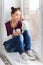 Teenage girl sitting on windowsill with smartphone