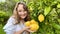 a teenage girl is standing near a lemon tree she is holding a lemon in her hands she is sniffing it she is going to make