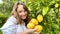 a teenage girl is standing near a lemon tree she is holding a lemon in her hands she is sniffing it she is going to make