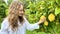 a teenage girl is standing near a lemon tree she is holding a lemon in her hands she is sniffing it she is going to make