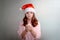 A teenage girl stands at home with a Santa hat and holds a burning white candle in her hands