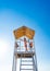 Teenage girl stands on lifeguard tower on beach against cloudless sky