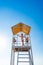 Teenage girl stands on lifeguard tower on beach against cloudless sky