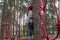 A teenage girl stands on a playground near a pine tree in rope parkour. Rope park for children in a pine forest.